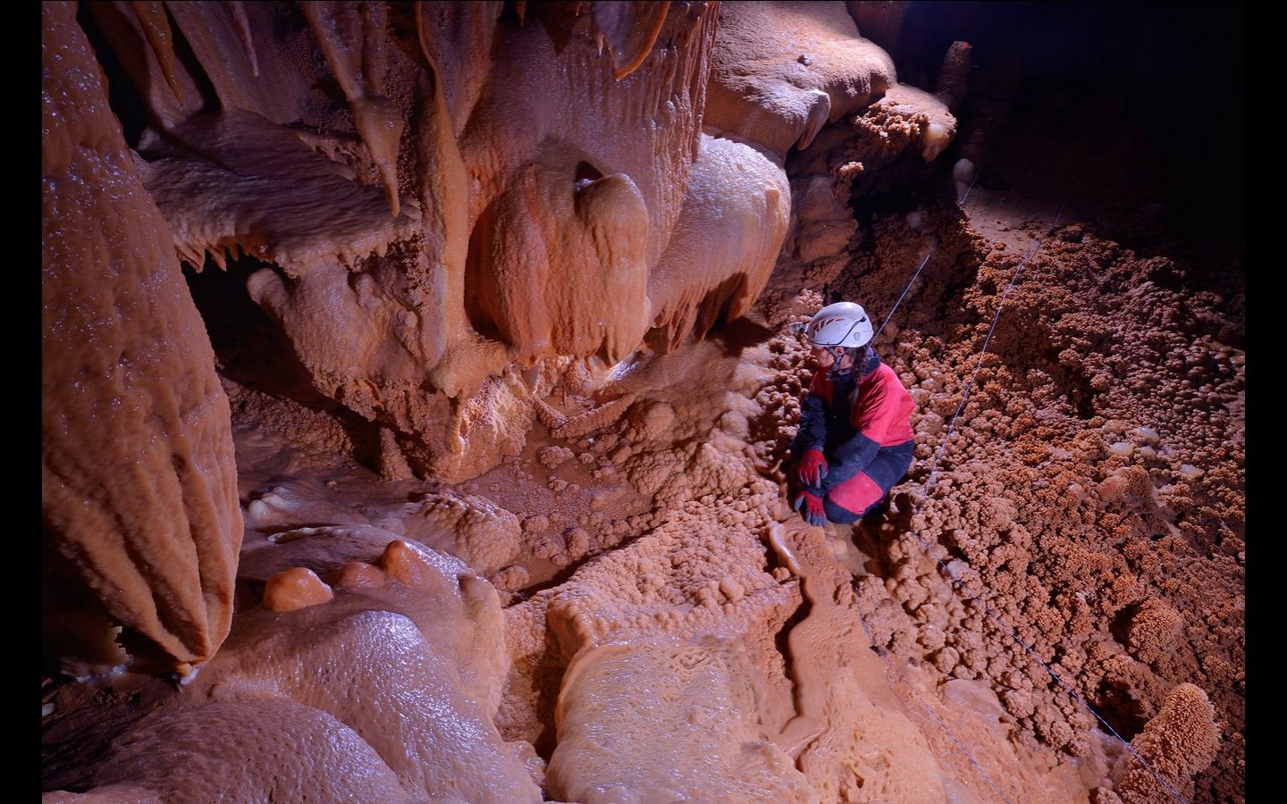 Une spéléologue accroupie au milieu de gours et de concrétions ocre
